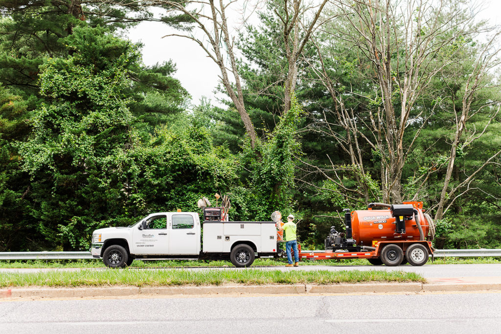 Workers stand next to a white company truck and attached equipment