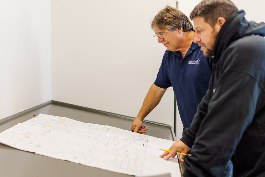 Two men stand while examining a paper blueprint