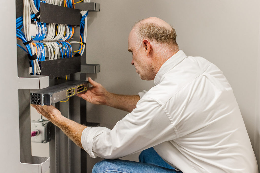 A worker kneels next to a communications system; cables visible