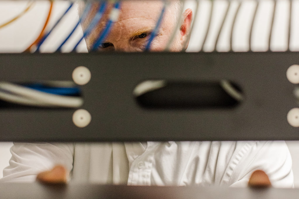 A man working on a server rack is visible through a slot and several wires