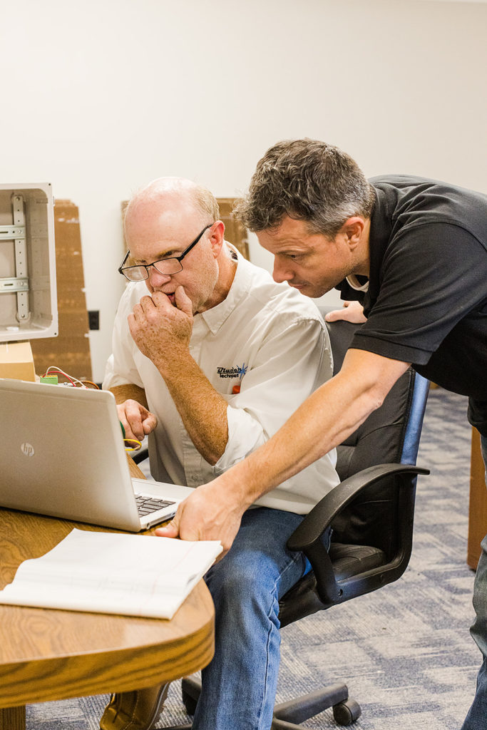 Two men work on a laptop computer (one standing and one sitting)