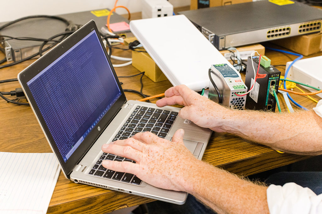 Someone works on a laptop with electronic devices and cables visible nearby